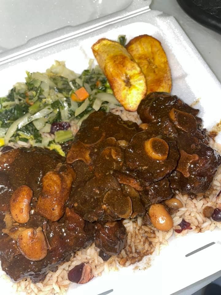 Takeout meal with rice, braised meat and mushrooms, salad, and fried plantains in a foam container