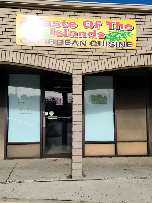 Storefront with a bright sign reading “Taste of the Islands Caribbean Cuisine” above glass doors and windows.
