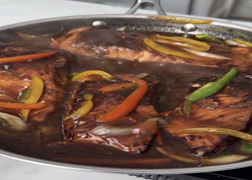 Close-up of glazed meat with sliced peppers and onions in a pan