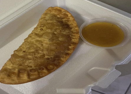 A fried crescent pastry in a foam takeout box with a small cup of dipping sauce