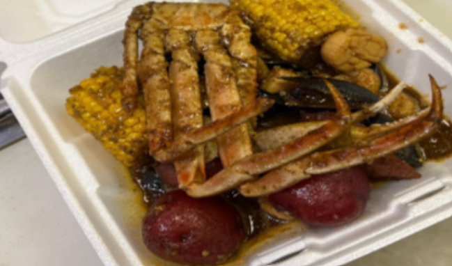 Seafood boil in a takeout container with crab legs, corn, potatoes, and seasoned sauce