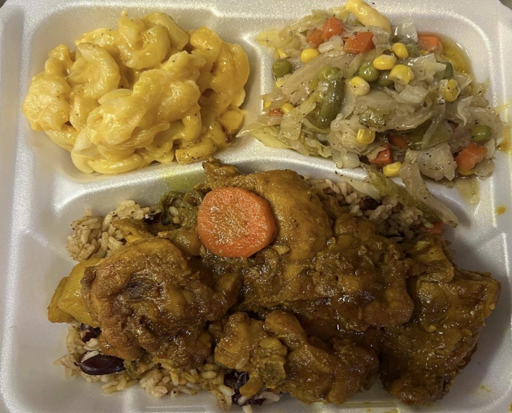 Three-compartment takeout tray with macaroni and cheese, mixed vegetables, and saucy meat with a carrot slice.