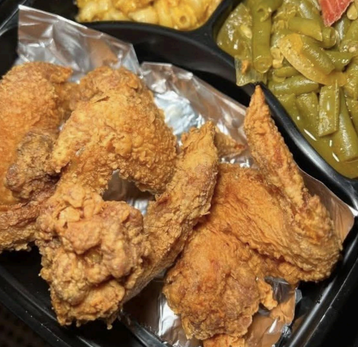 Fried chicken pieces in a takeout tray with green beans and macaroni and cheese in the background