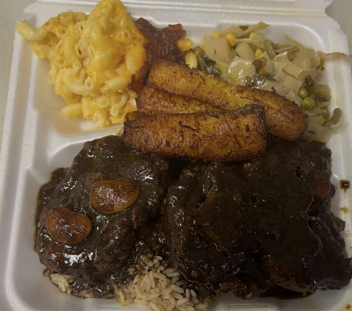 Takeout tray with macaroni and cheese, fried fish, collard greens, and dark sauced meat over rice