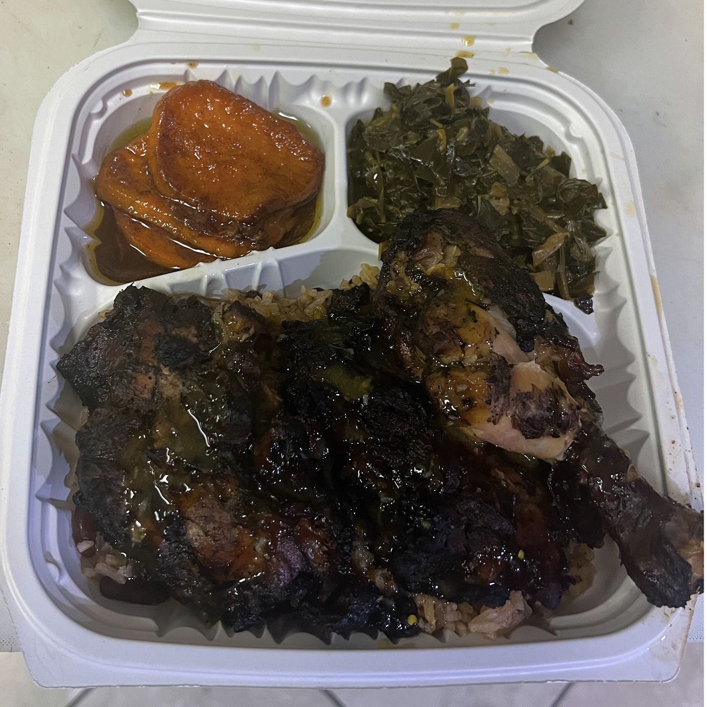 Takeout container with glazed chicken, rice, and collard greens