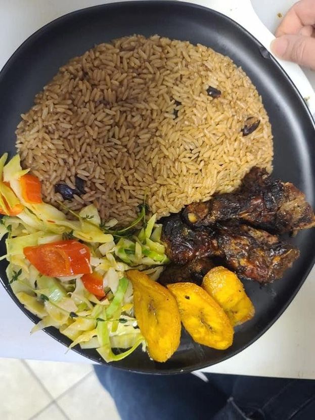 Plate with brown rice, grilled meat, fried plantains, and mixed vegetables on a black dish