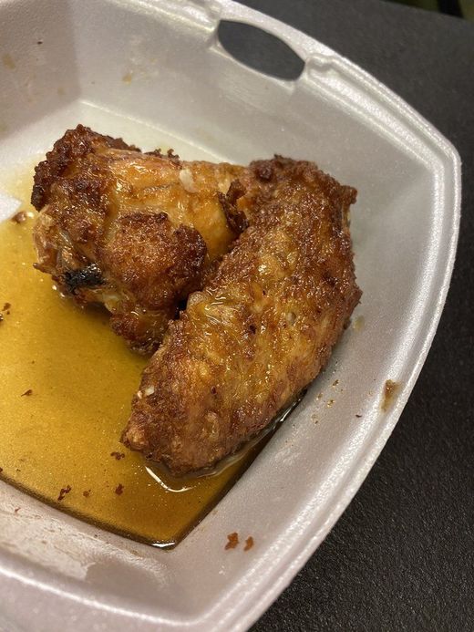 Two pieces of fried chicken in a foam takeout container with a pool of sauce