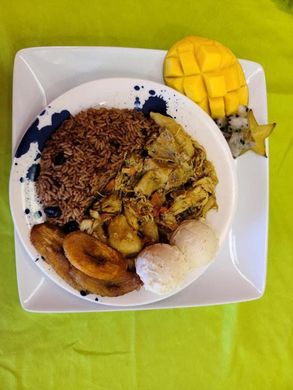 Plate of rice, curried vegetables, fried plantains, and mango on a square white dish