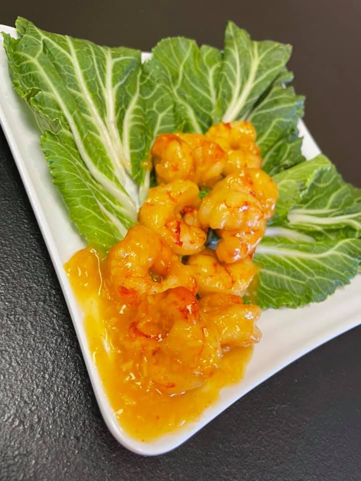 Shrimp in orange sauce served on green napa cabbage leaves on a white plate