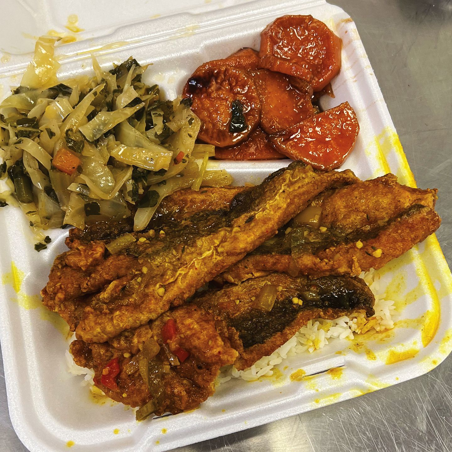 Takeout container with fried fish, sautéed greens, and sliced tomatoes