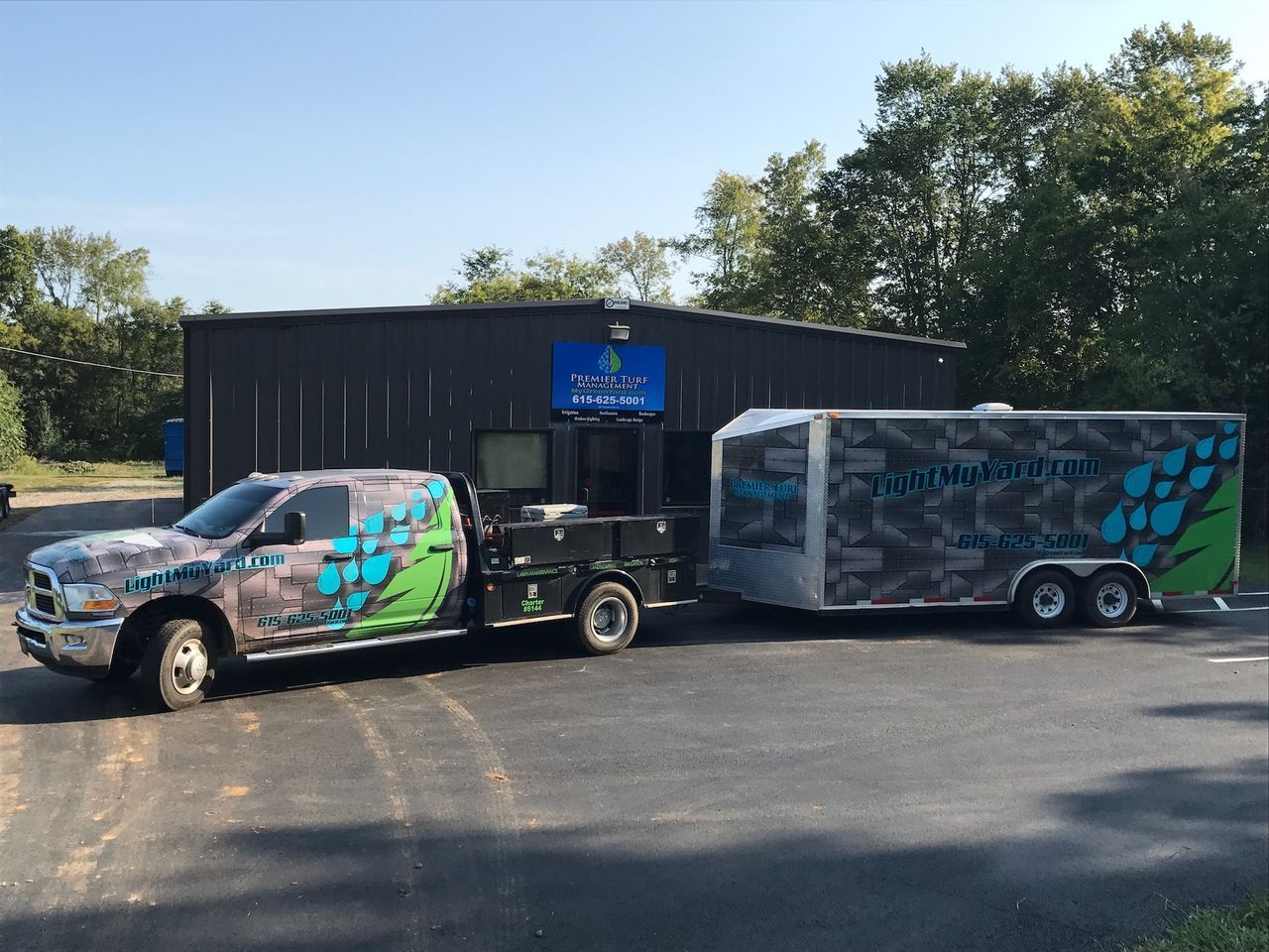 Custom-wrapped pickup truck with trailer parked outside a black building on a sunny day