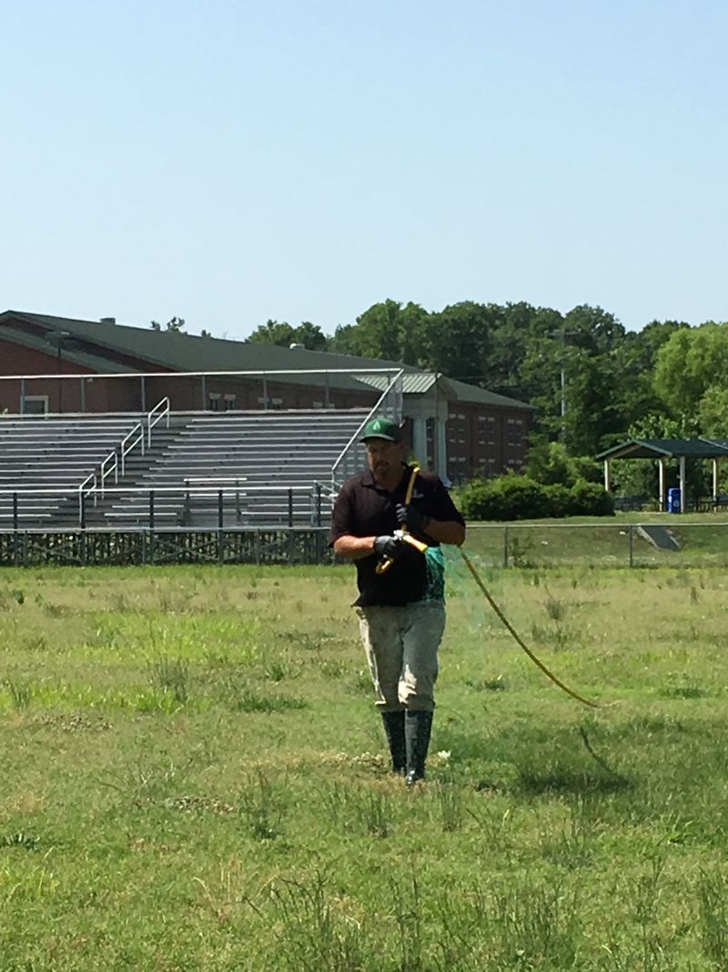 Person walking across a grassy field at a stadium, holding a long leash or cable.