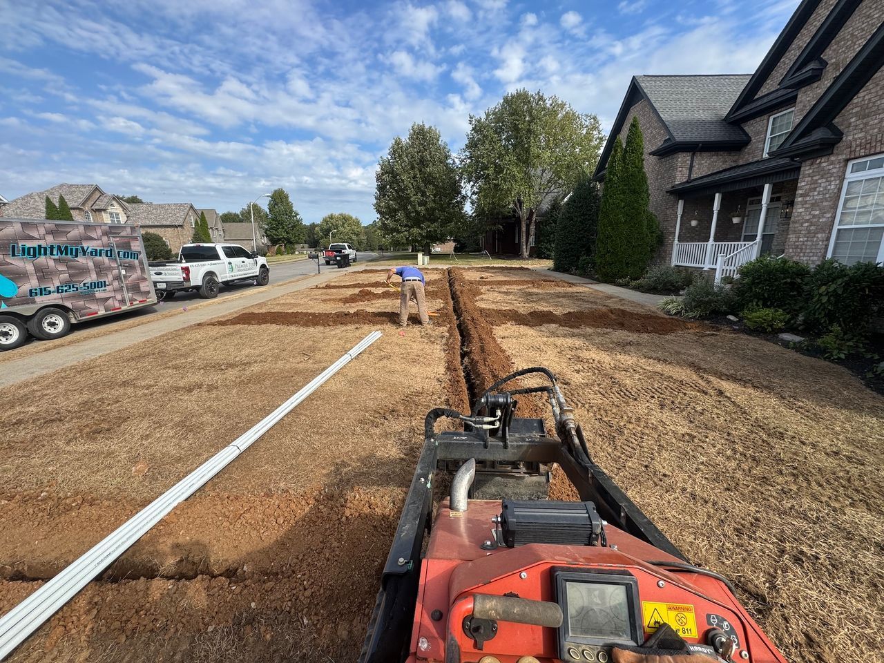 Trench digger cutting a narrow trench in a suburban yard beside a house and dirt driveway