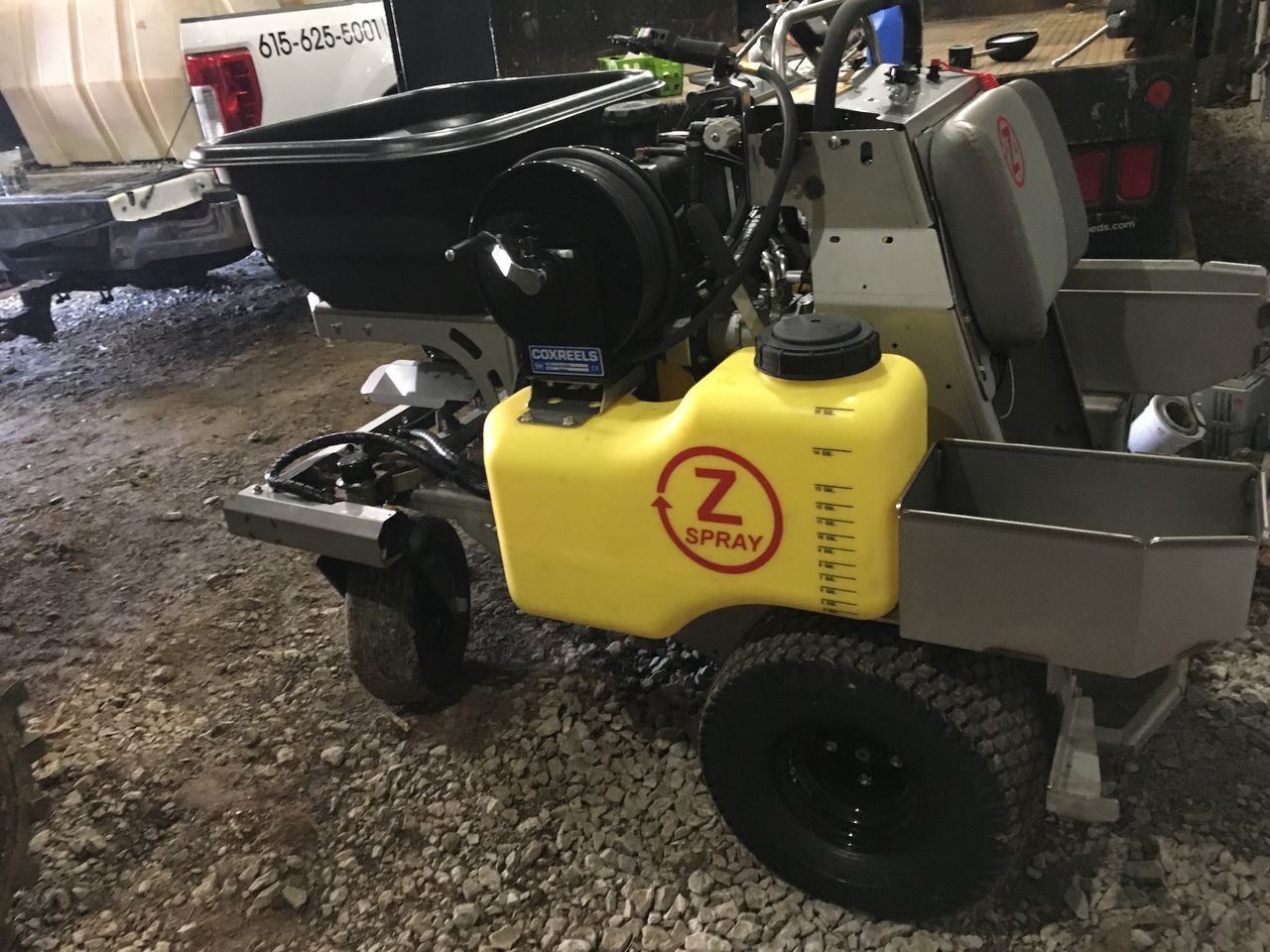 Yellow utility cart with a black seat and storage bins, parked on a gravel surface in a garage.