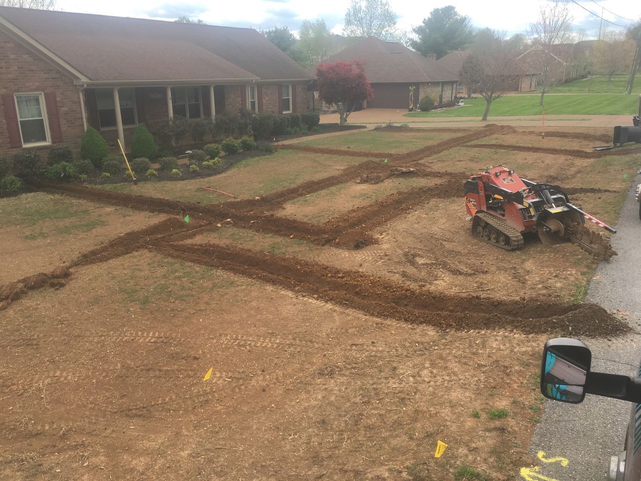 Front yard with fresh dirt landscaping, a brick house in back, and a red ATV parked on the right.