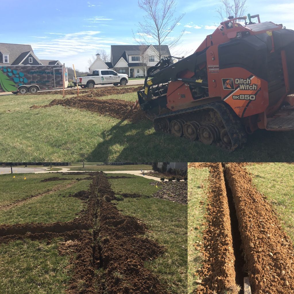 Orange excavator trenching a lawn in a suburban yard, with soil piled along the cut path.