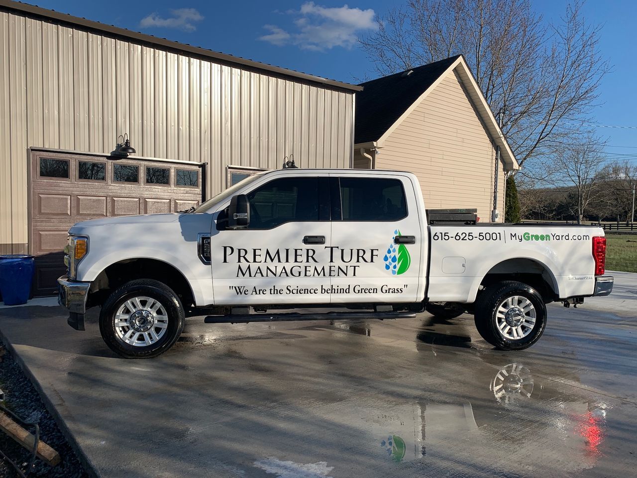 White Premier Turf truck parked outside a beige building on a sunny day.