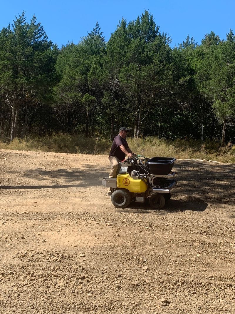 Person riding a yellow ATV across a dry dirt field with trees in the background