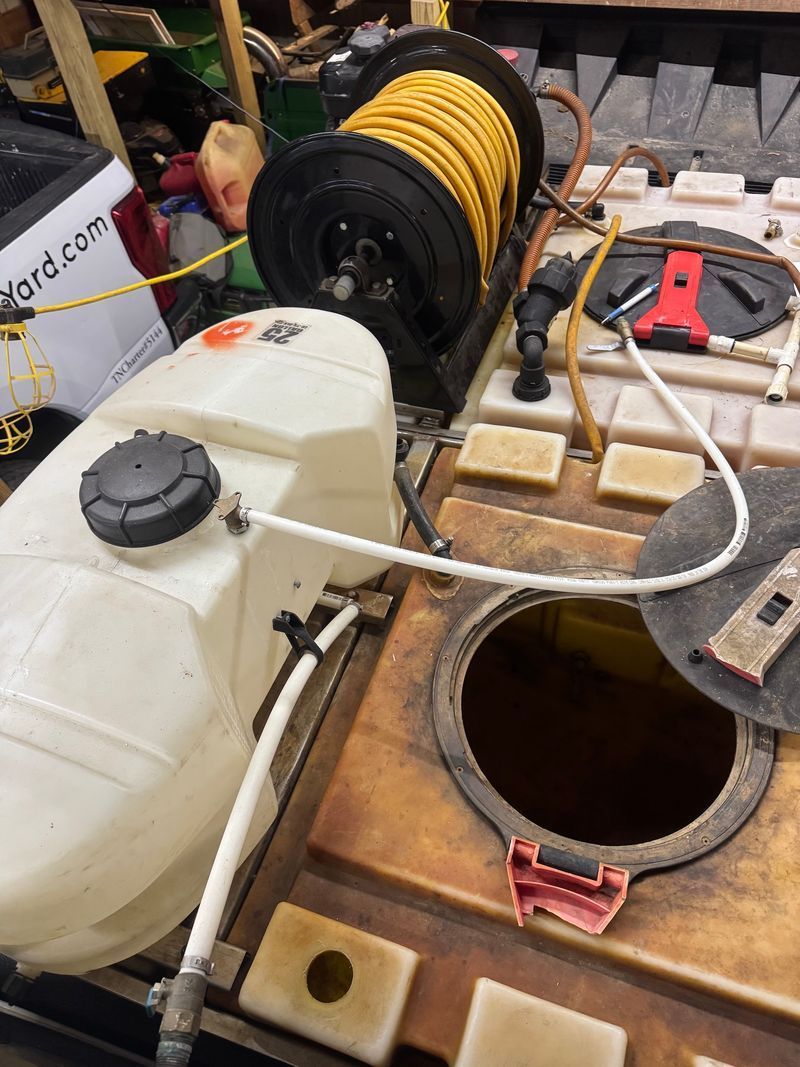 Model boat deck with white tank, hose, yellow rope reel, and open hatch in a workshop