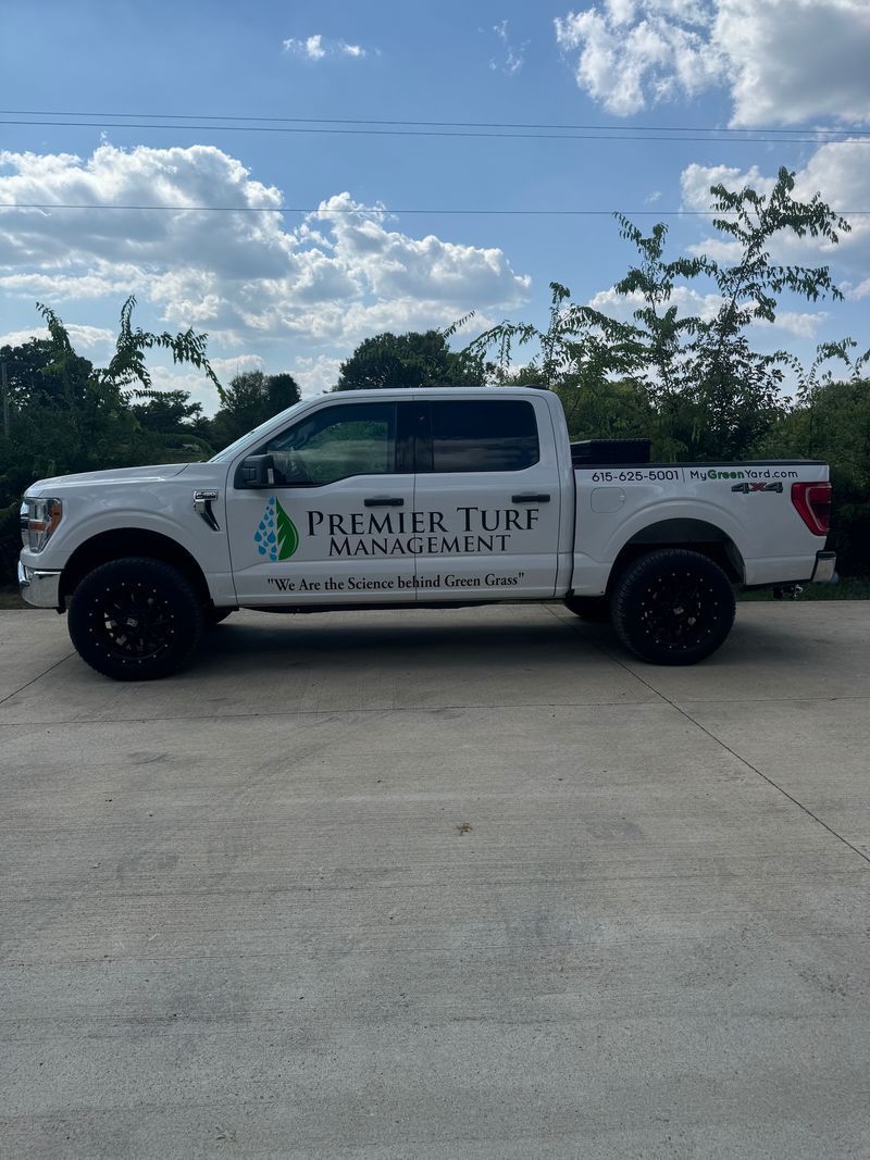 White pickup truck with black wheels and company logo, parked on pavement under a blue sky.