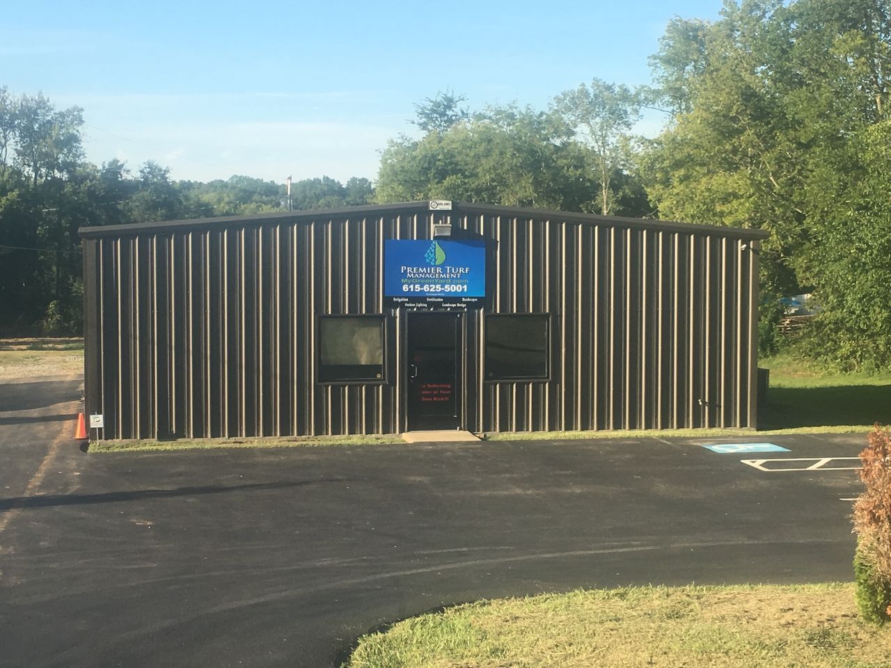Small striped roadside building with blue sign, set beside an empty paved lot and trees.