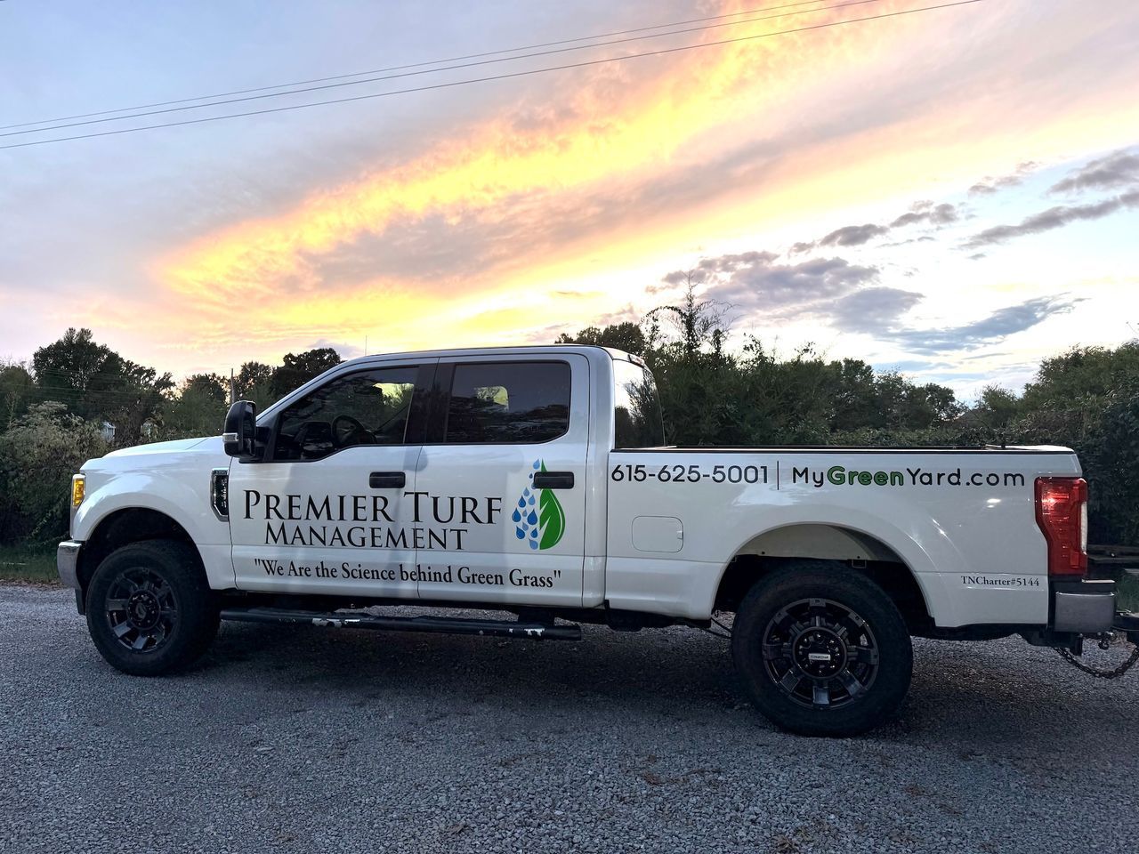 White Premier Turf Management pickup truck parked outdoors at sunset under a colorful sky