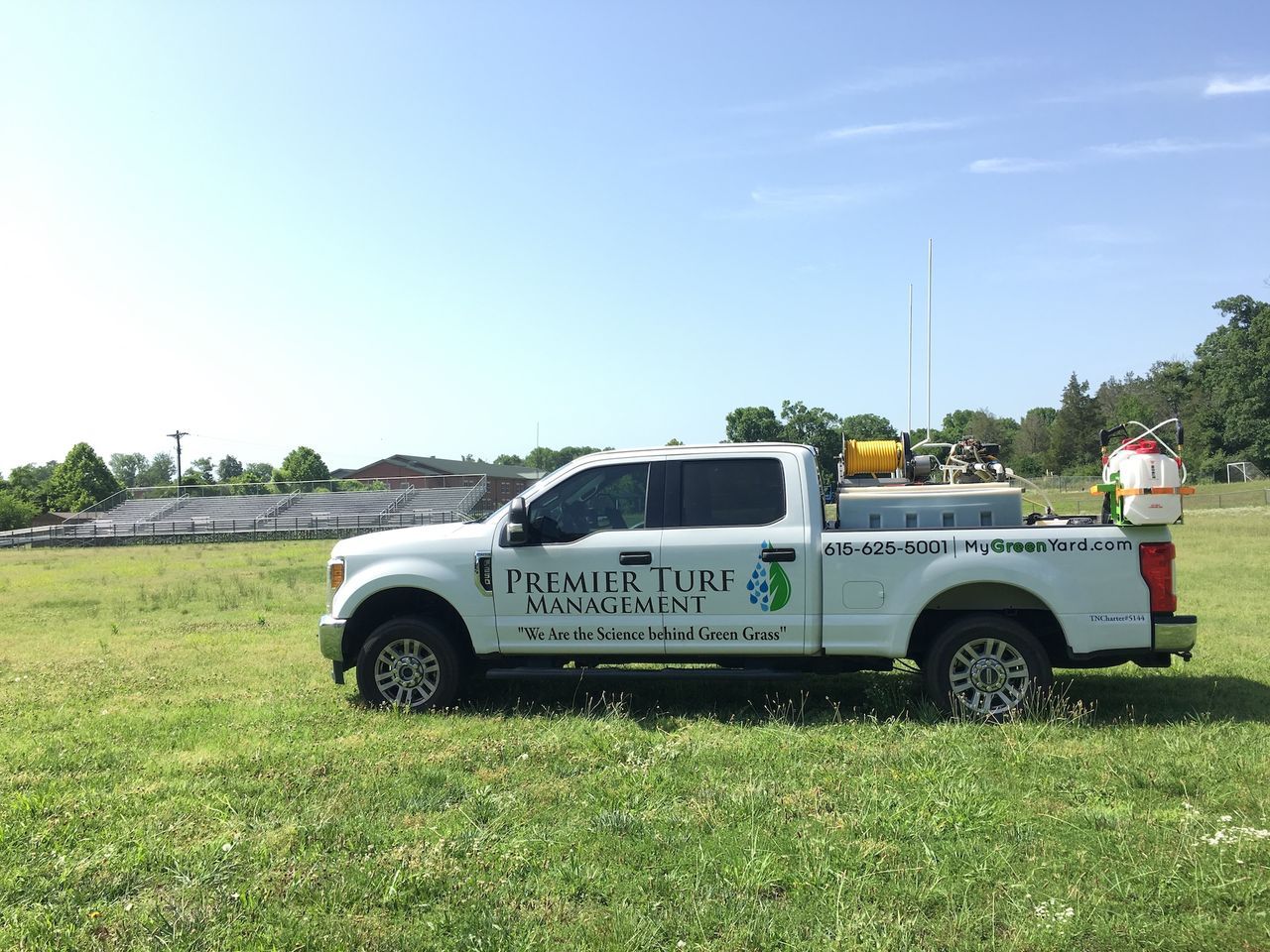 White utility truck with logo parked in a grassy field under a blue sky