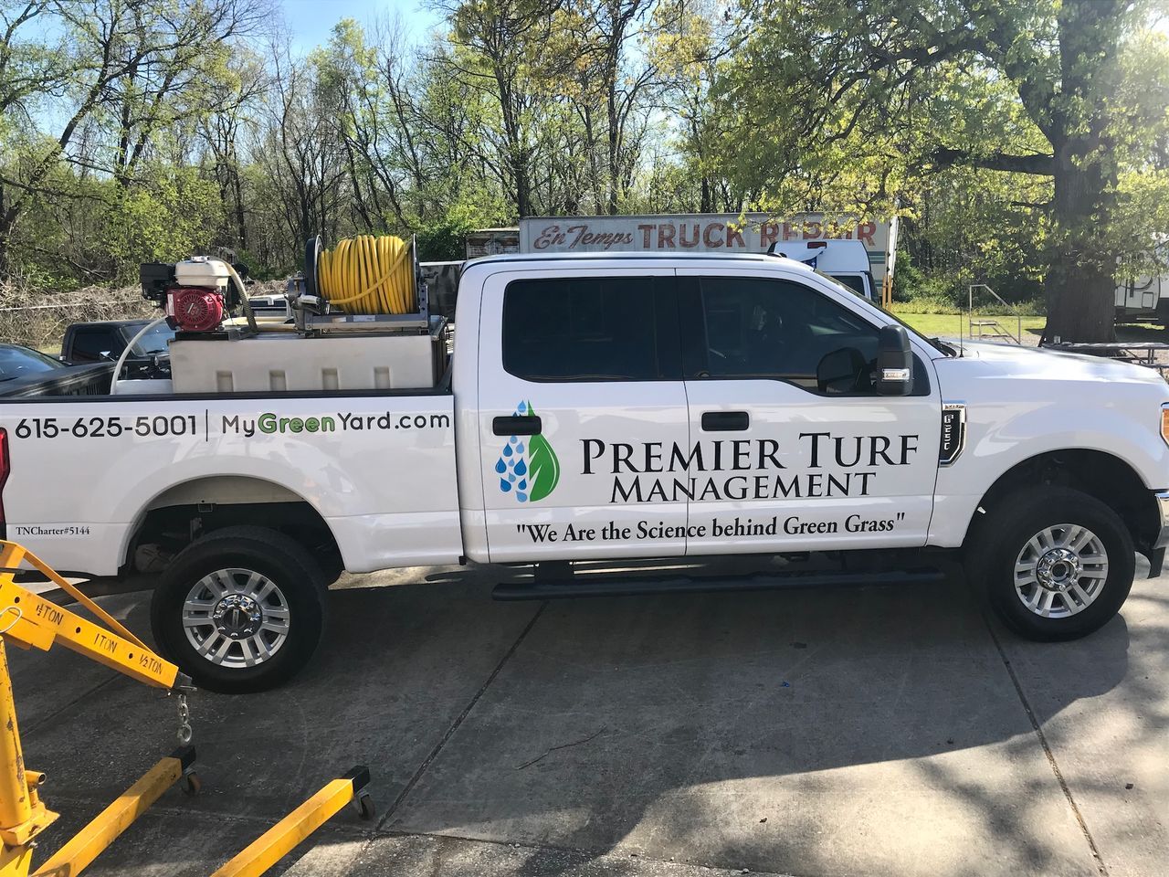 White Premier Turf Management pickup truck parked outdoors with landscaping equipment attached