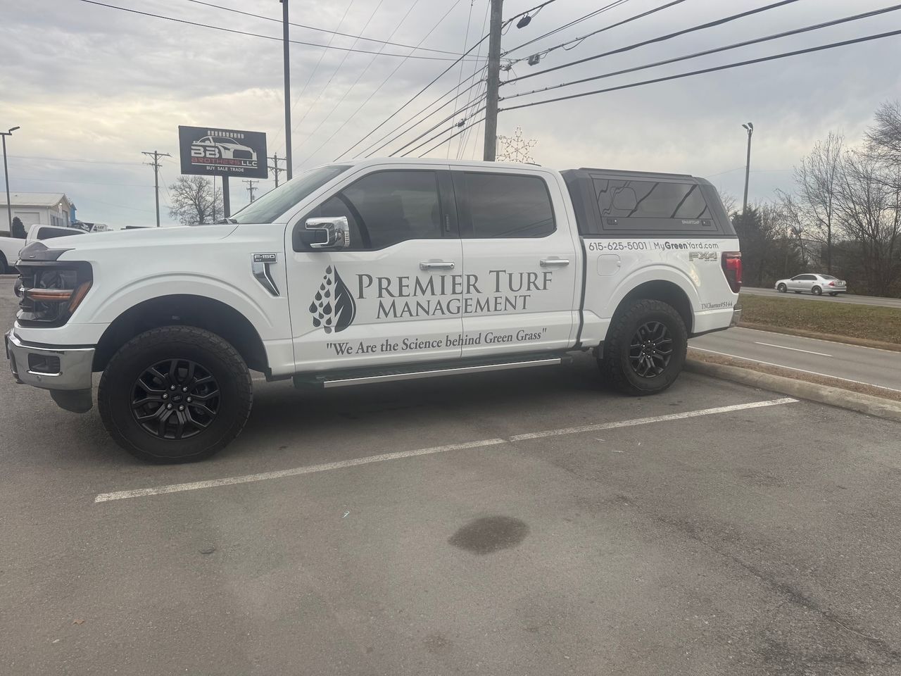 White Premier Turf Management pickup truck parked roadside near an intersection