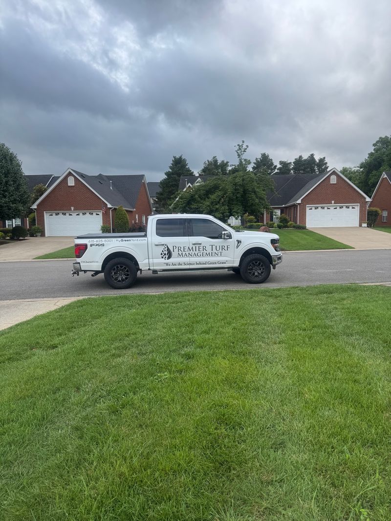 White pickup truck parked on a suburban street beneath cloudy skies, with brick houses in the background