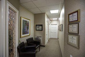Hallway with waiting room furniture and framed art and certifications.