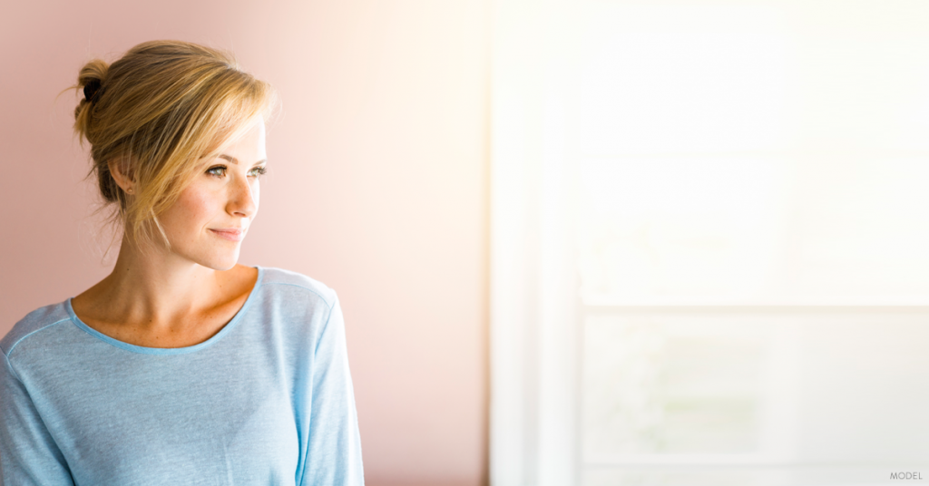 Blonde woman looking out a window, wearing a light blue sweater.