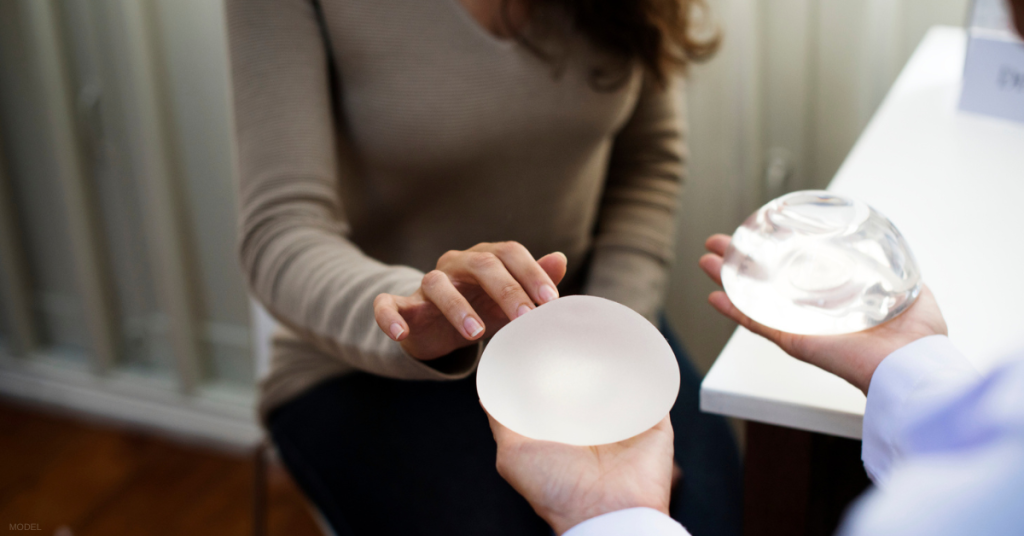 A person looking at breast implants held by a healthcare provider in a consultation room.