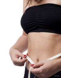 Woman in black top measuring waist with a tape measure.