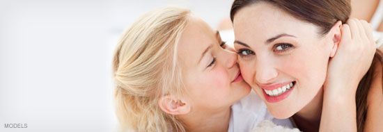 A young girl kisses a woman's cheek. The woman smiles. Both are indoors.