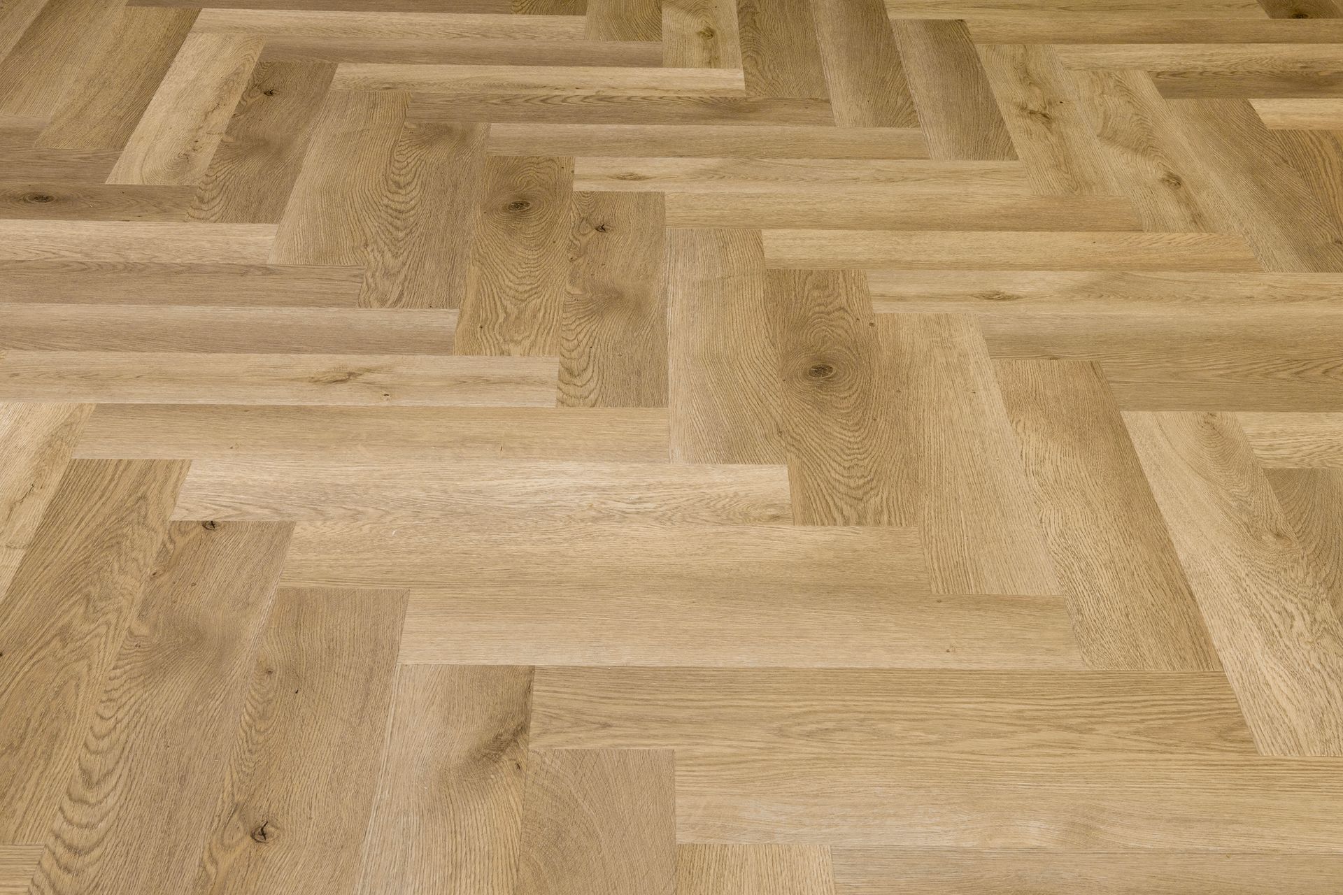 Primer plano de un suelo de madera clara con diseño de espiga.