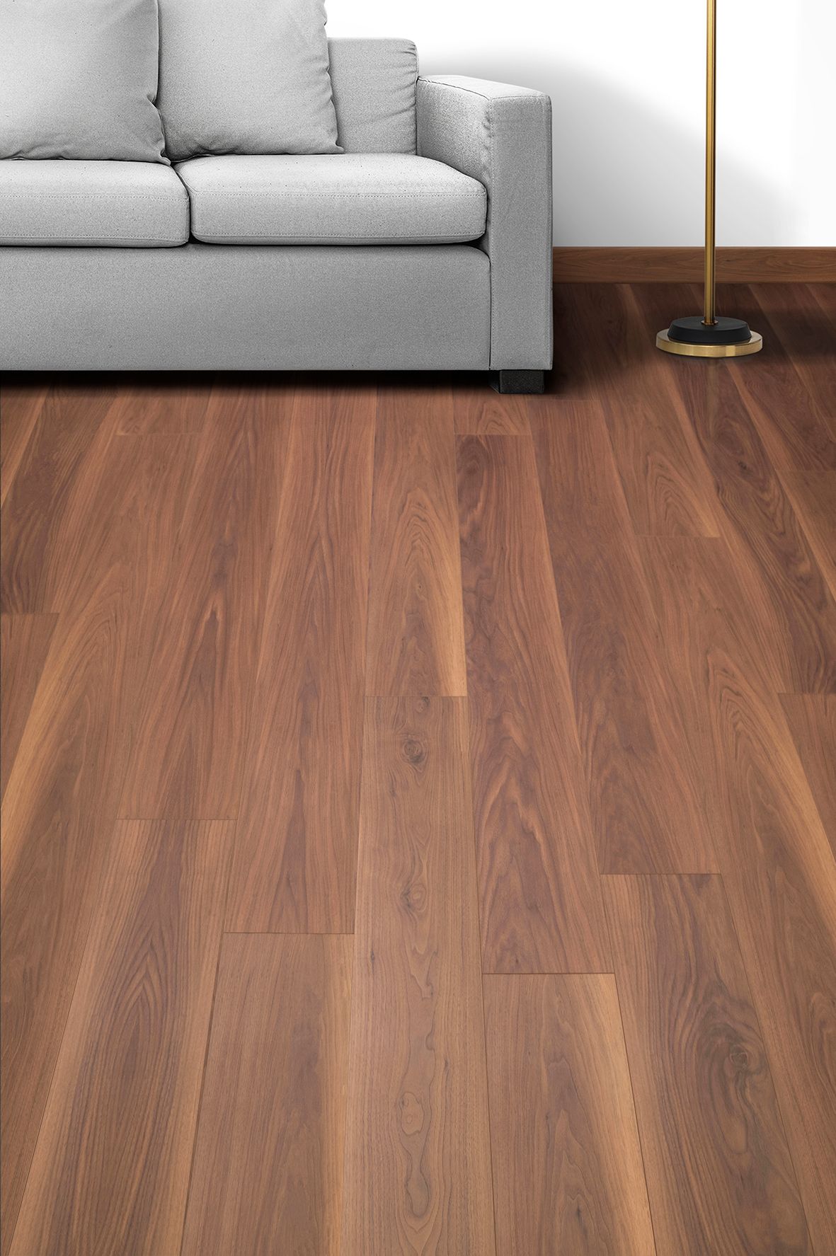 Sofá gris y lámpara de pie de latón sobre un suelo de madera en un salón minimalista.