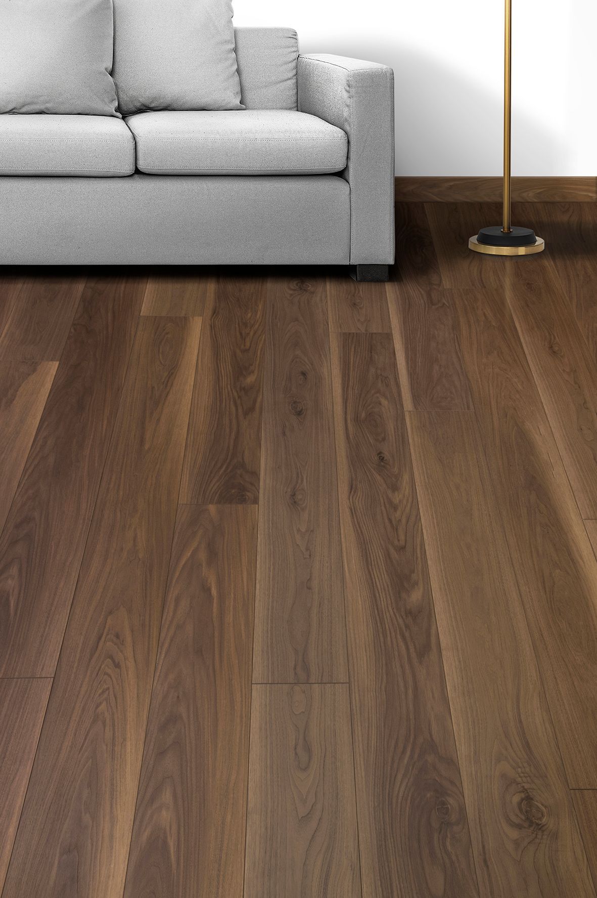 Sala de estar con sofá gris y suelo de madera oscura, además de una lámpara de pie dorada.