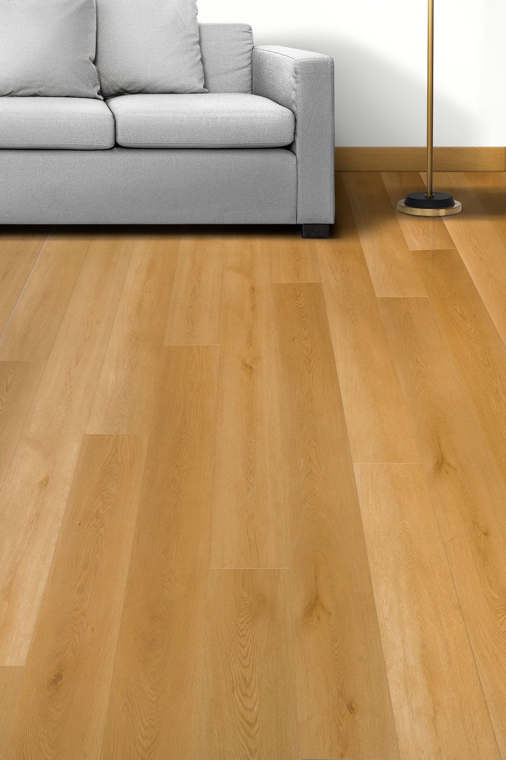 Suelo de madera clara junto a un sofá gris y una lámpara de pie en un salón luminoso.