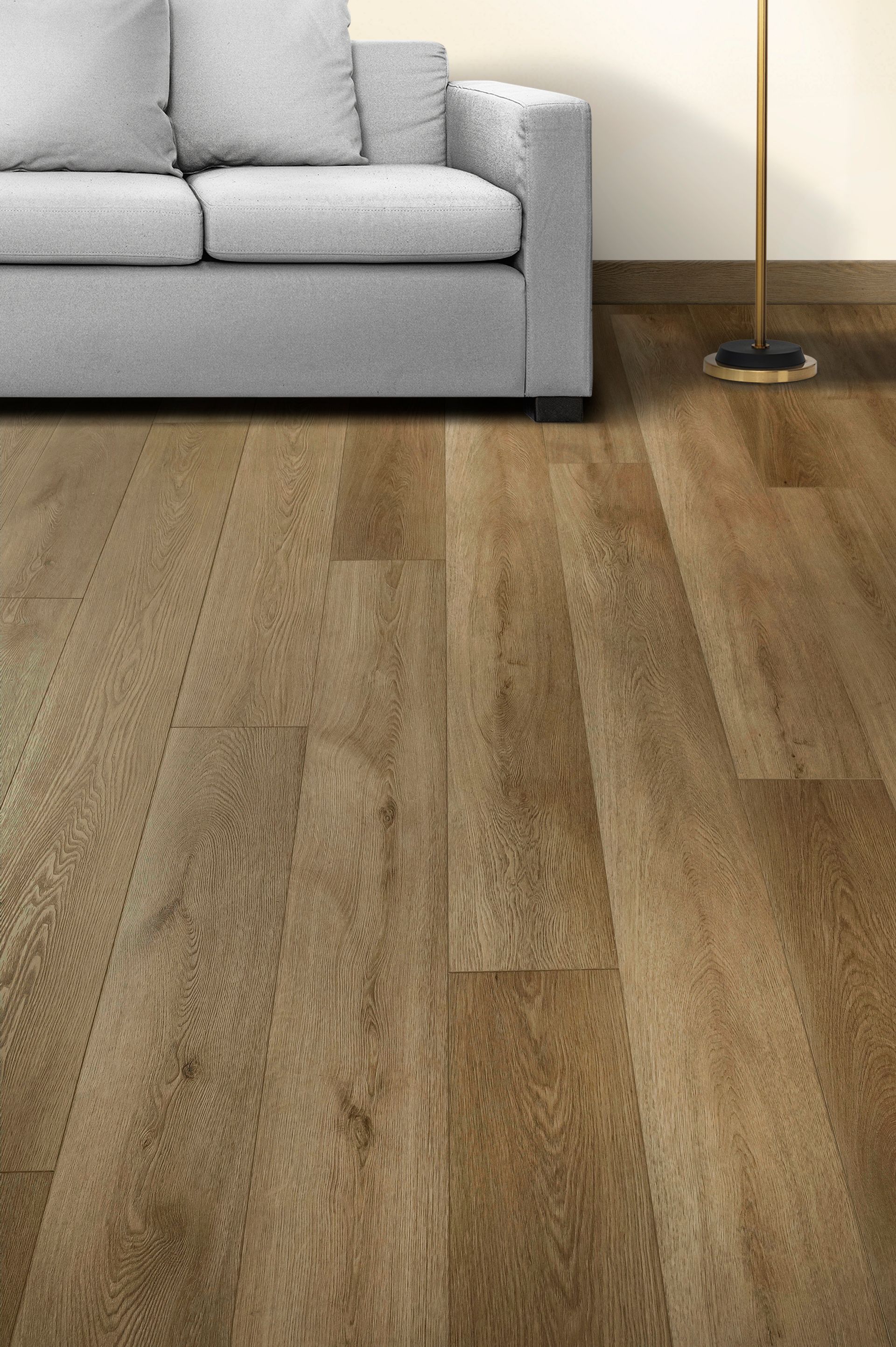 Sala de estar con sofá gris claro, suelo de madera y lámpara de pie contra una pared blanca.