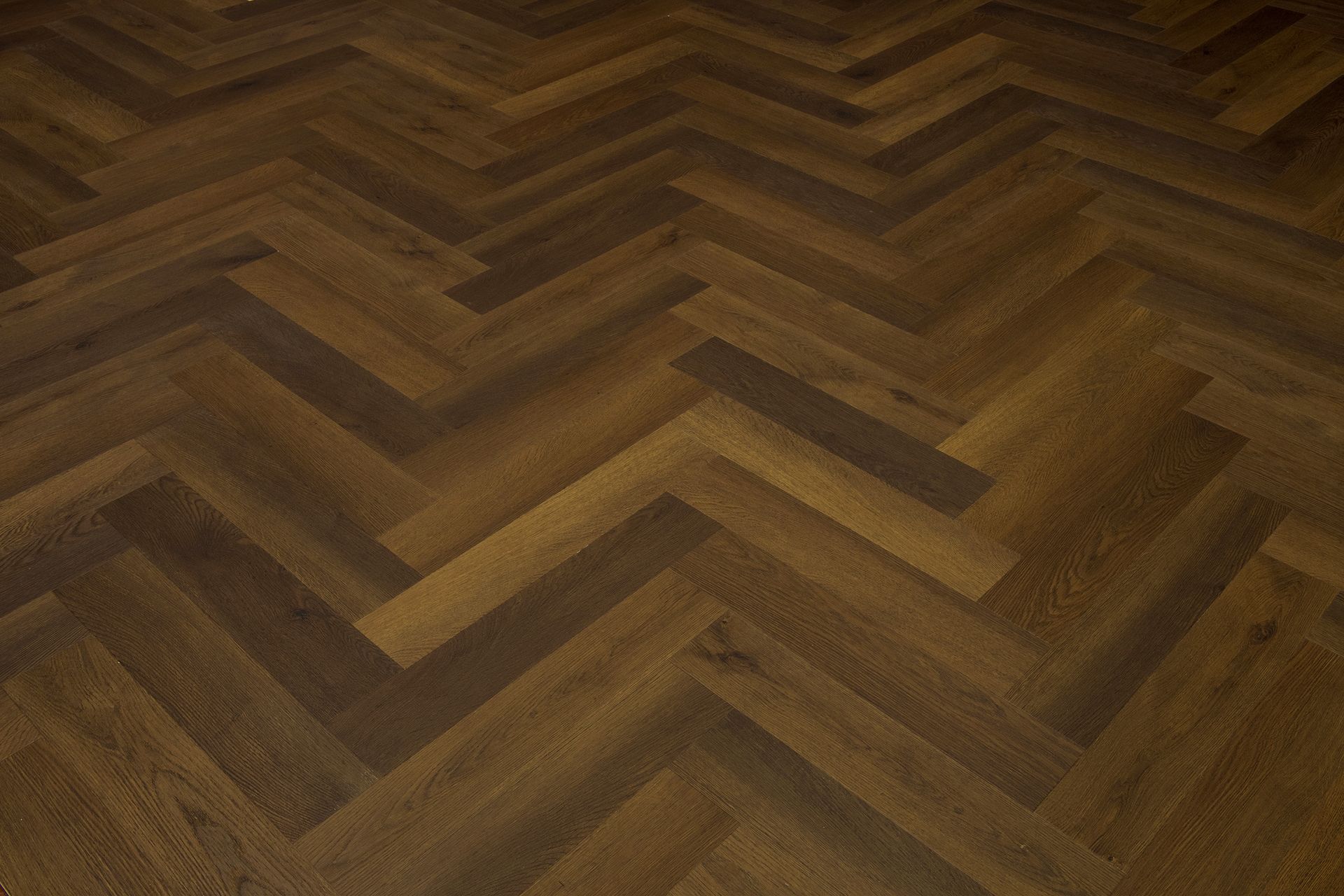 Suelo de madera en espiga en tonos marrones cálidos, mostrado en primer plano.