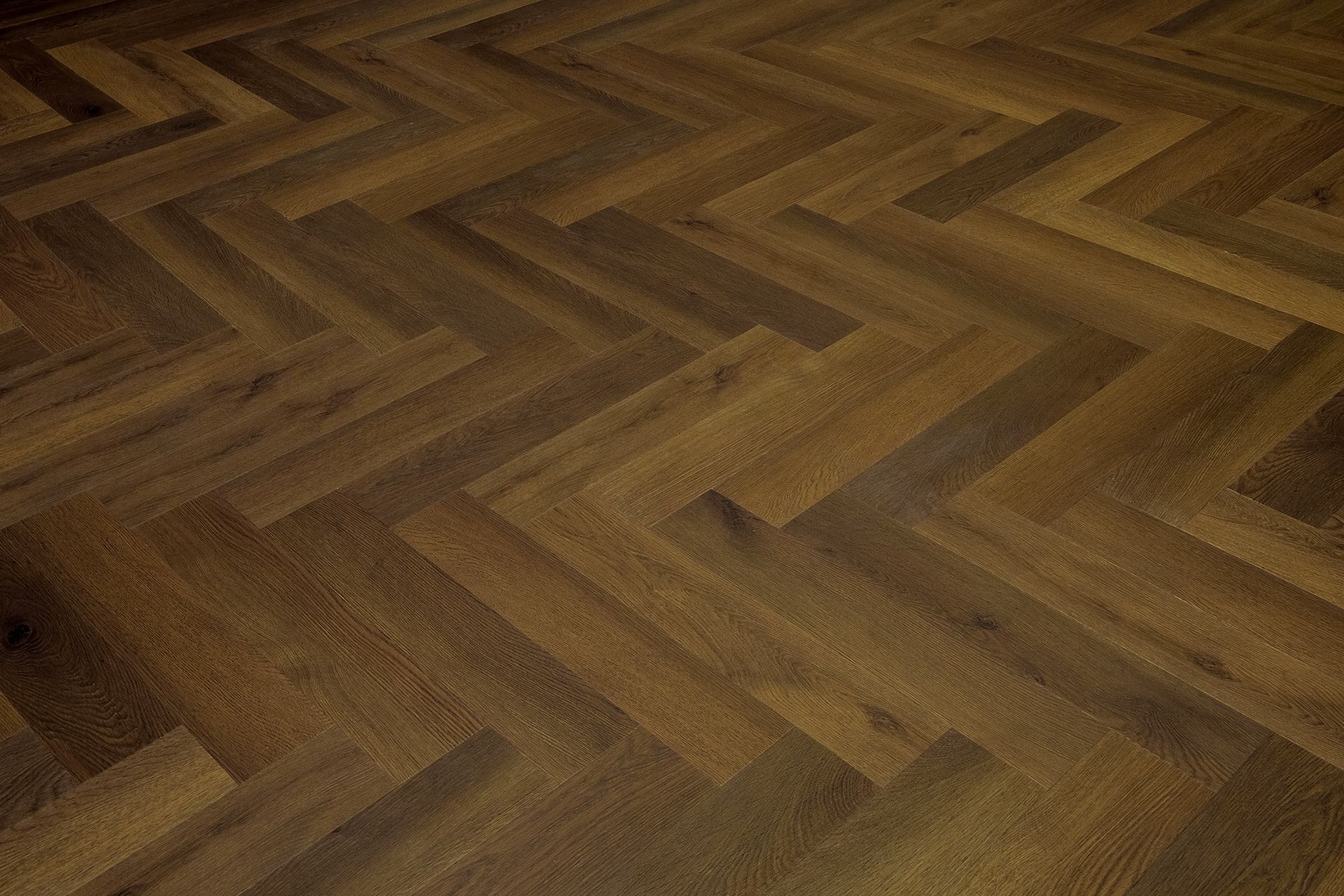 Primer plano de un suelo de madera en espiga en tonos marrones cálidos.