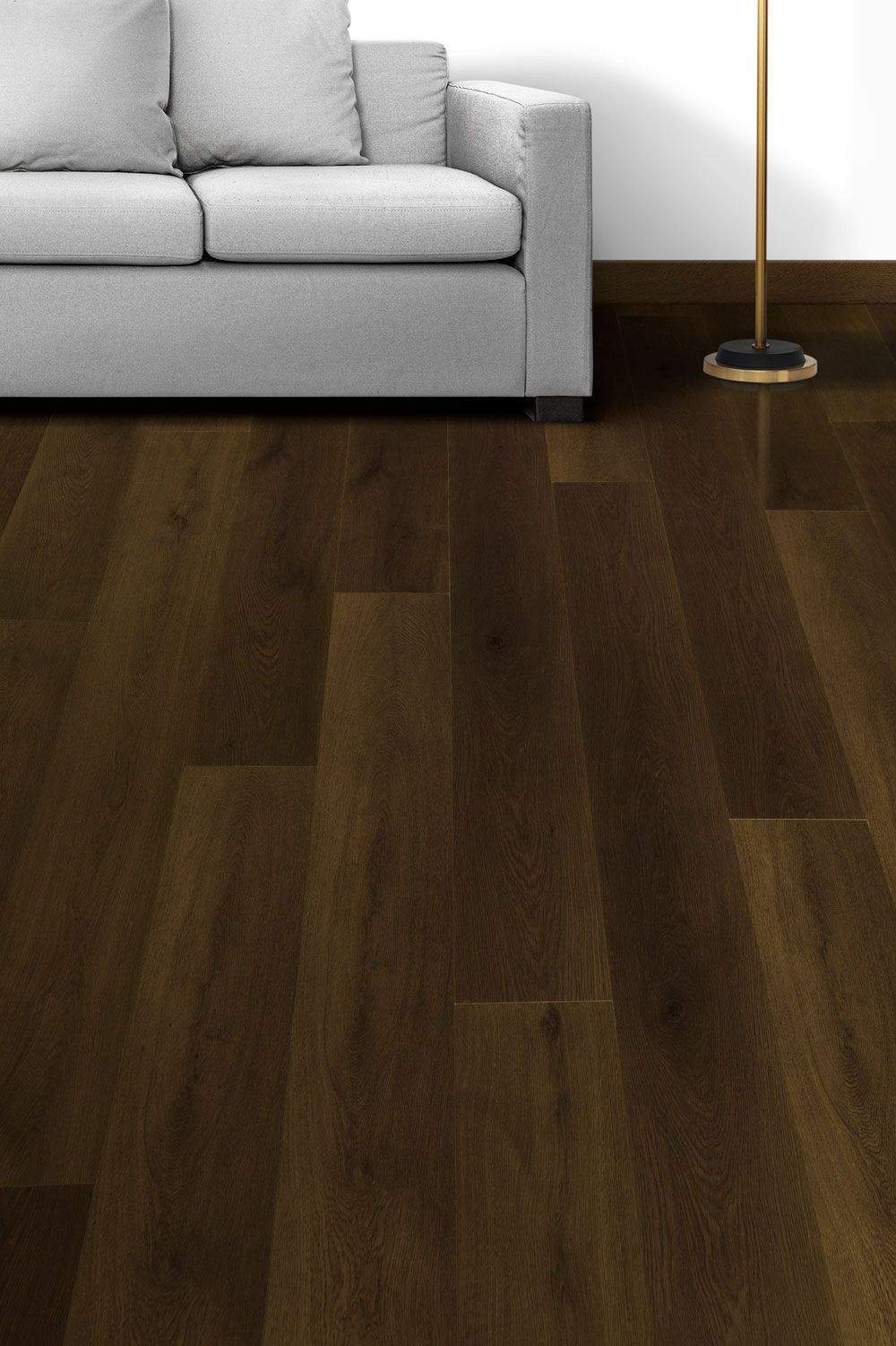 Sofá gris claro junto a una lámpara de pie sobre suelo de madera oscura en una habitación minimalista.