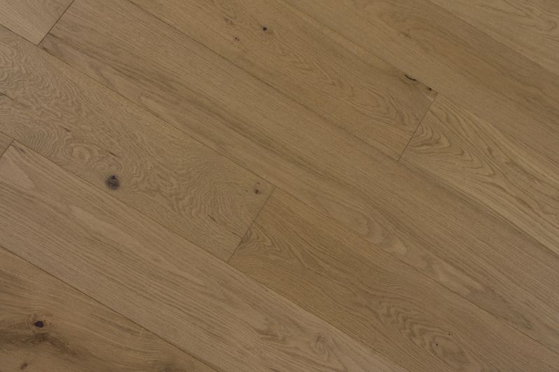 Primer plano de un suelo de madera clara con vetas diagonales y un pequeño nudo oscuro.