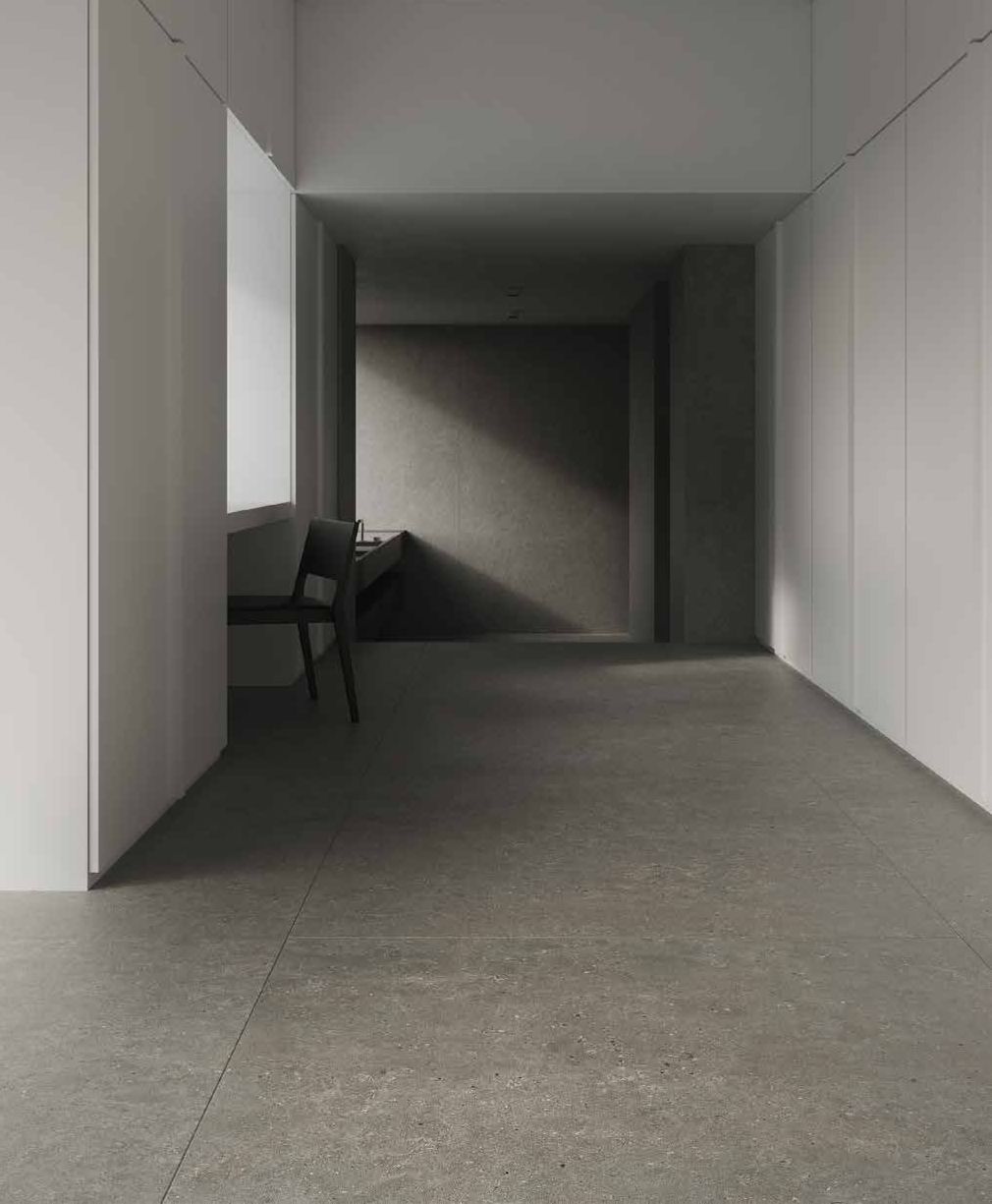 Pasillo moderno y vacío con paredes y suelo grises, y una silla arrimada a la pared izquierda.