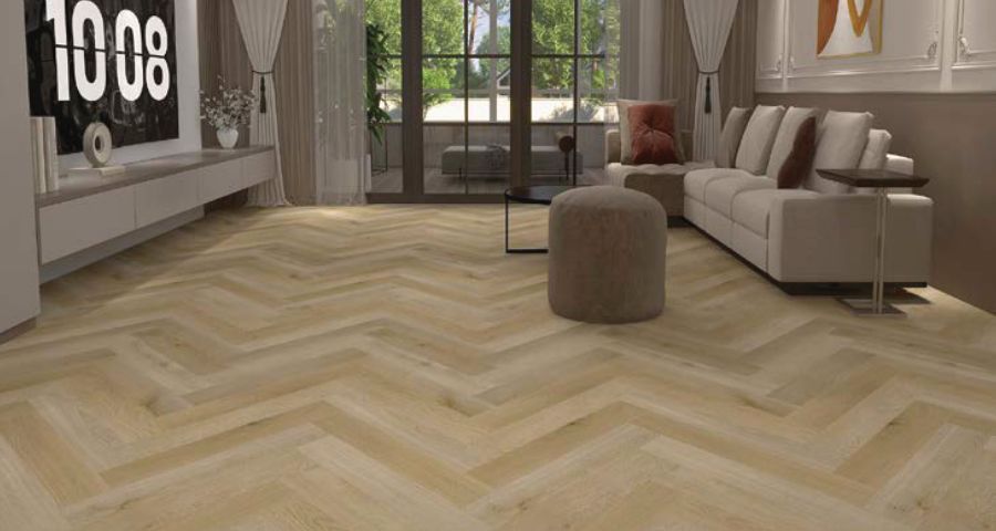 Sofá azul sobre una alfombra beige con estampado de espiga en una sala de estar luminosa.