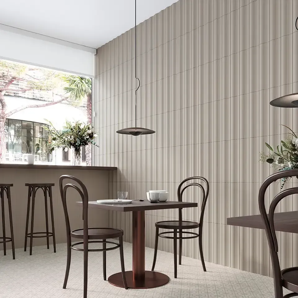 Interior de cafetería moderna con mesas de madera, sillas de madera curvada, lámparas colgantes y paneles de pared con rayas verticales.