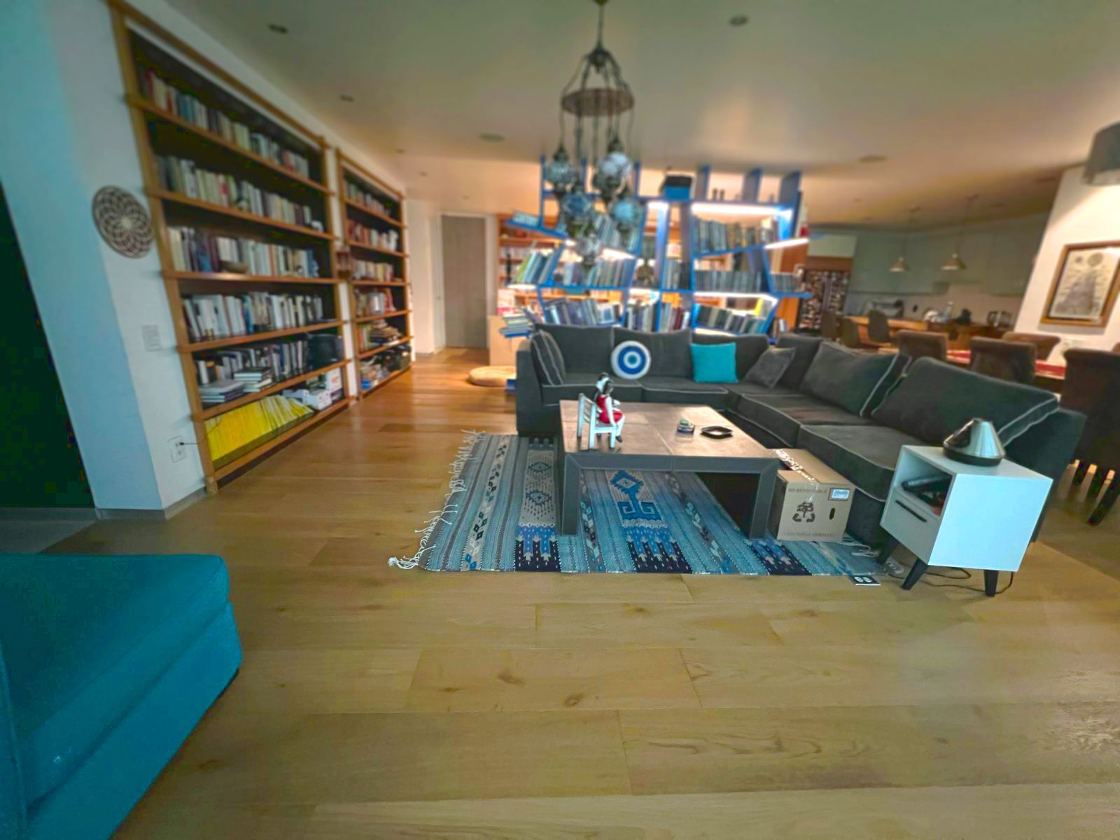Amplio salón moderno con suelos de madera, sofás azules, estanterías y una mesa de centro con lámpara.