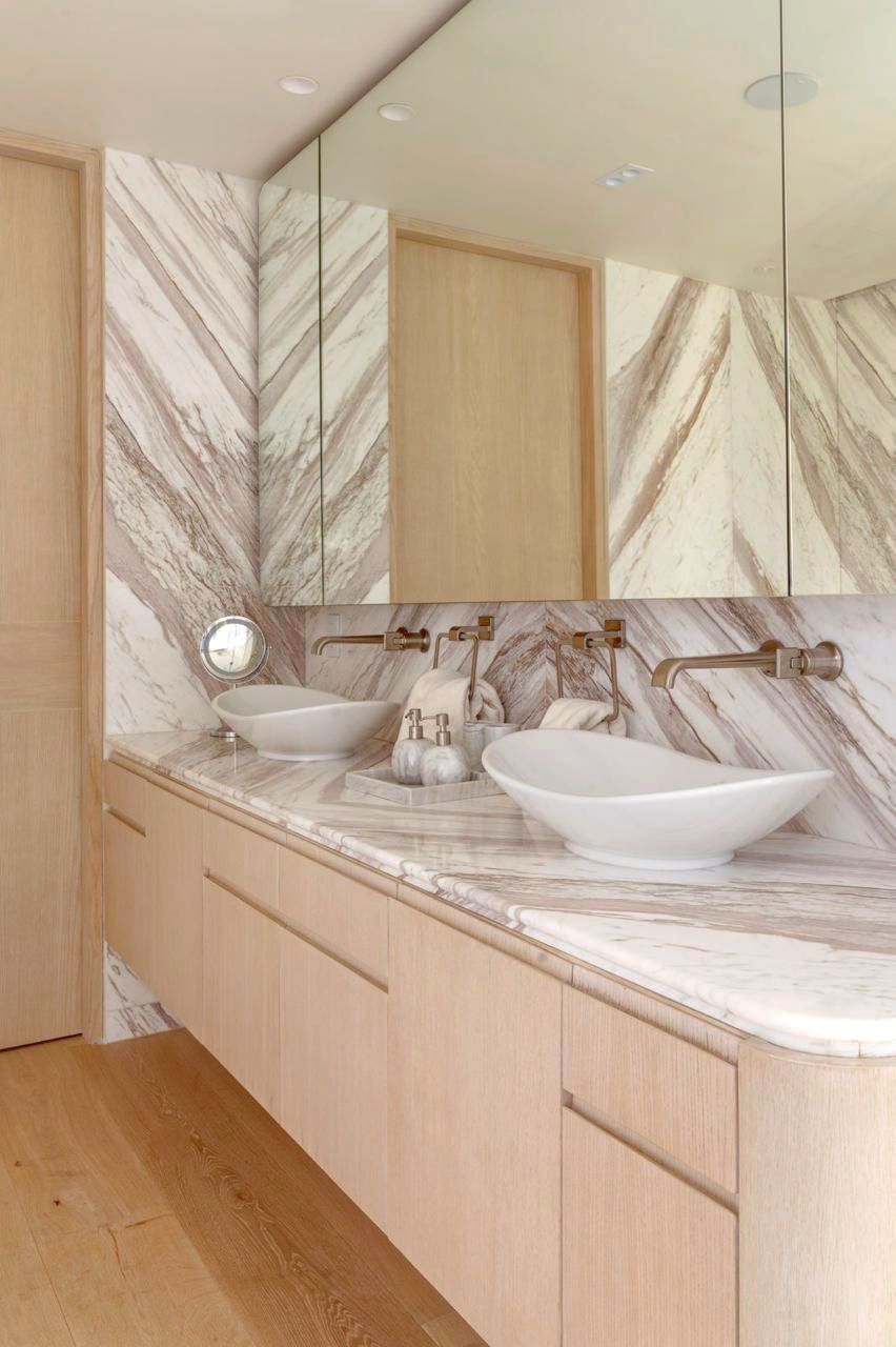 Tocador de baño moderno con lavabos dobles, encimeras de mármol y gabinetes de madera en un diseño luminoso y minimalista.