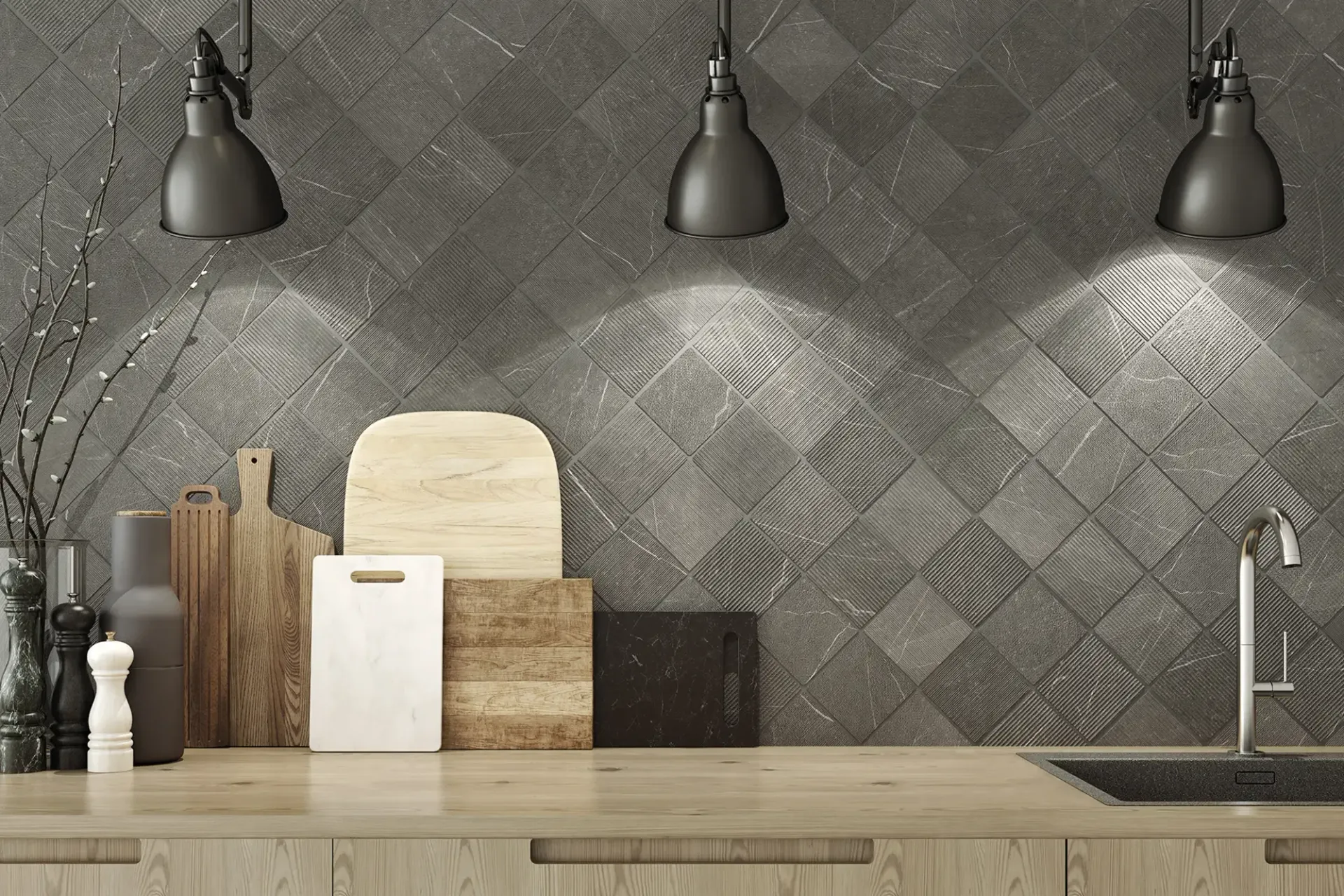 Encimera de cocina moderna con salpicadero de azulejos grises, tres lámparas colgantes, tablas de cortar y grifo de fregadero.